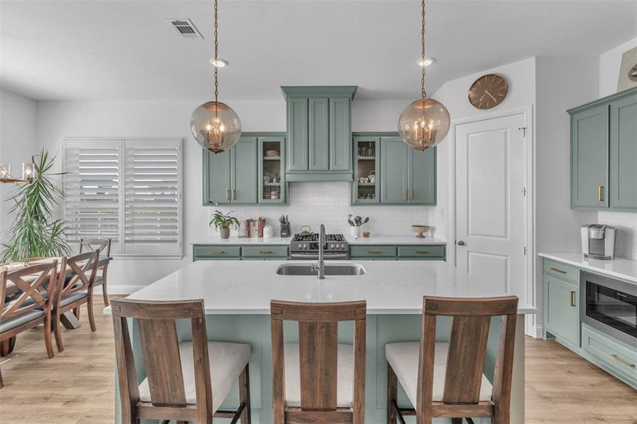 Kitchen with green cabinetry, light hardwood / wood-style floors, sink, and decorative light fixtures