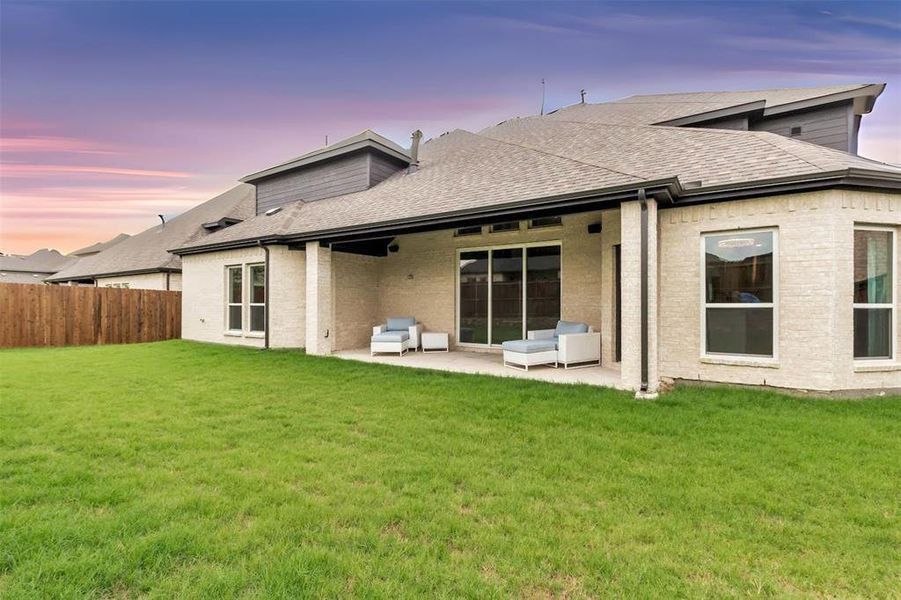 Back house at dusk featuring a patio and a lawn