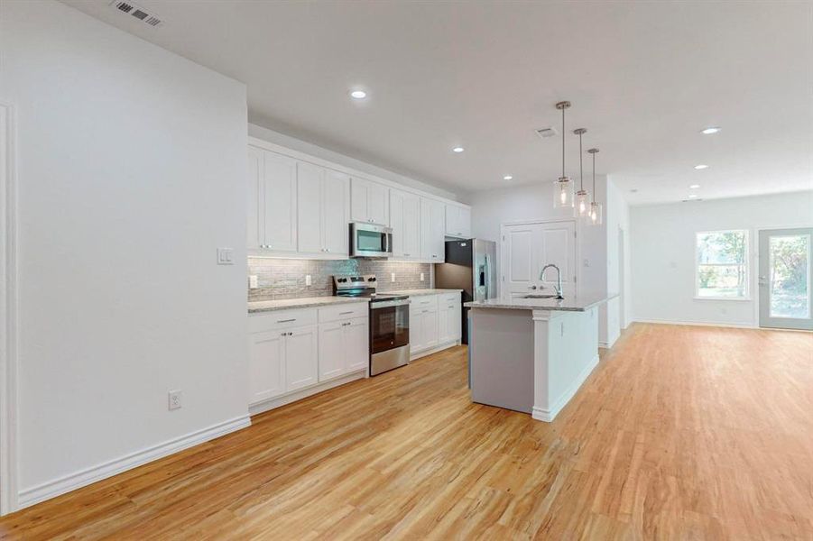 Un-staged Kitchen with pendant lighting, light wood-type flooring, a kitchen island with sink, white cabinets, and appliances with stainless steel finishes