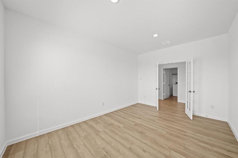 The Office/study has white French doors with glass panels with fresh white walls and wood flooring, featuring recessed lighting leading to the adjoining home.