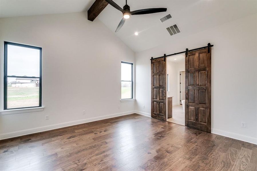 Spare room featuring a barn door, lofted ceiling with beams, dark hardwood / wood-style flooring, and a healthy amount of sunlight