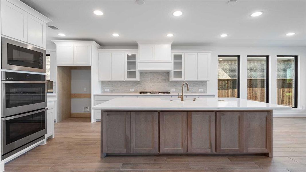 Kitchen with sink, an island with sink, white cabinetry, stainless steel appliances, and light hardwood / wood-style flooring