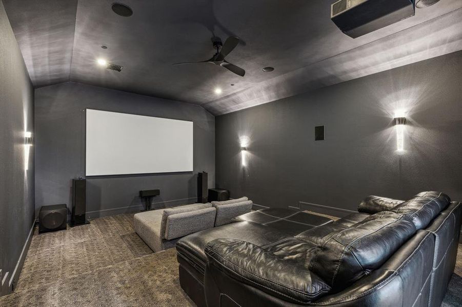 Home theater room featuring ceiling fan, dark carpet, and lofted ceiling