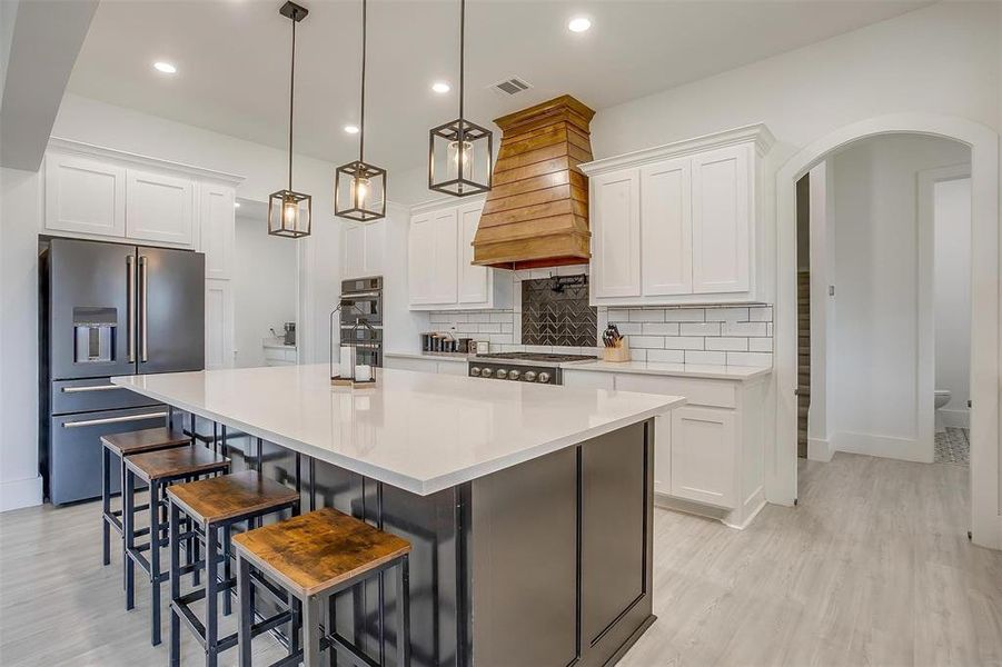 Kitchen featuring appliances with stainless steel finishes, decorative backsplash, light wood-type flooring, and custom range hood