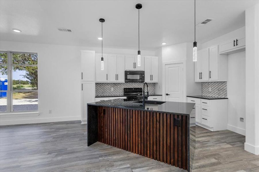 Kitchen with an island with sink, pendant lighting, stainless steel electric range, and white cabinets