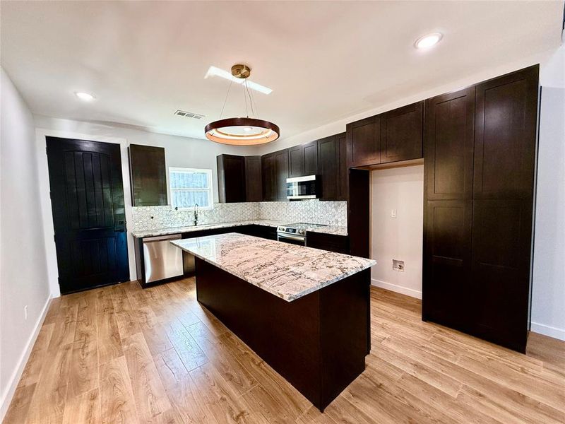 Kitchen with hanging light fixtures, appliances with stainless steel finishes, light wood-type flooring, dark brown cabinetry, and a center island