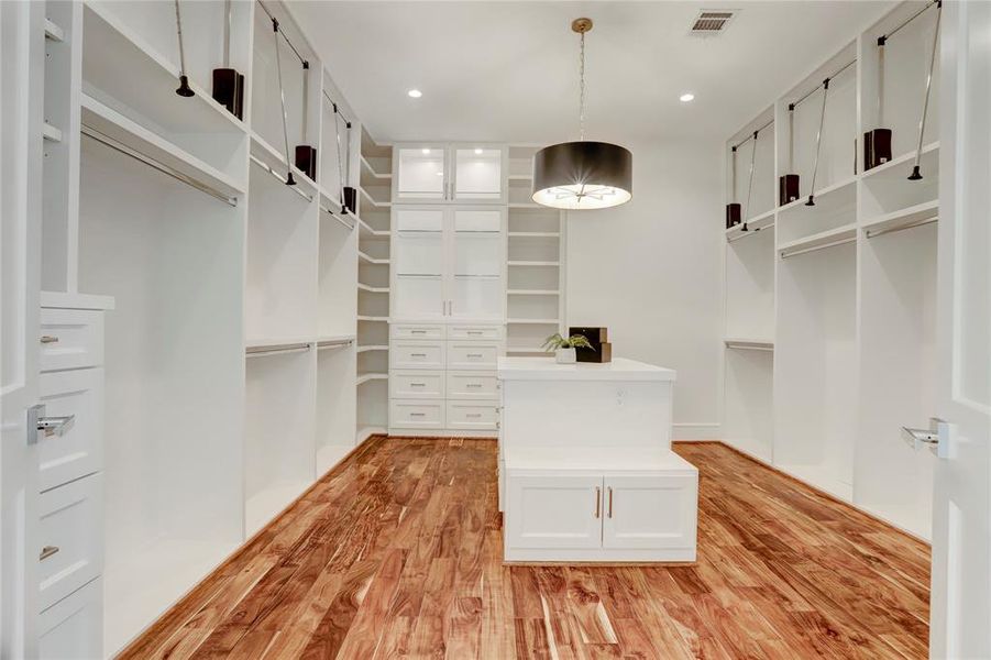 The Primary Closet has it all!  A built-in island with bench, an elegant black and brass chandelier, tons of hanging space, built-in shelving and chest of drawers and glass-front display cabinets with LED lights.