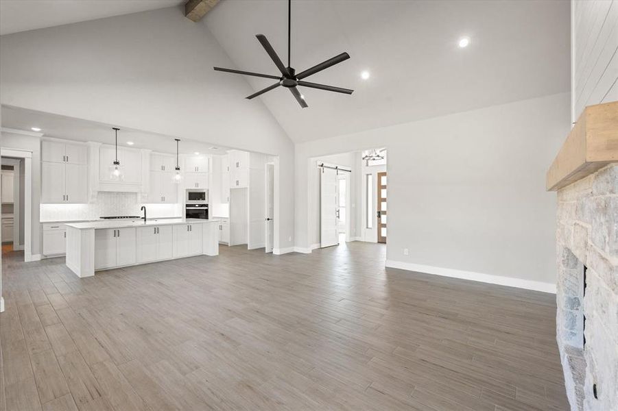 Unfurnished living room with a barn door, hardwood / wood-style floors, ceiling fan, beam ceiling, and high vaulted ceiling