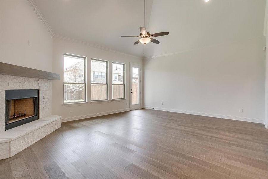 Unfurnished living room featuring ceiling fan, a brick fireplace, wood-type flooring, and ornamental molding