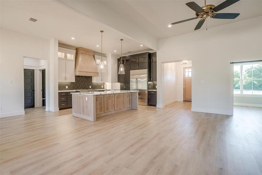 Kitchen featuring premium range hood, light hardwood / wood-style flooring, a kitchen island with sink, and pendant lighting