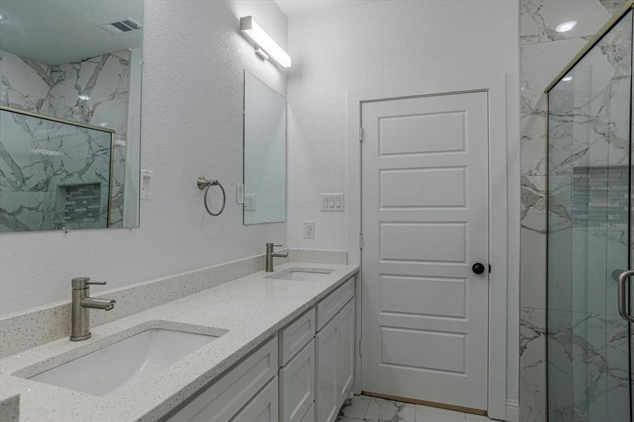 Bathroom with tile flooring, a shower with shower door, and double sink vanity