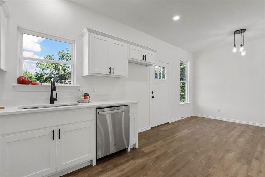 Kitchen featuring sink, dark hardwood / wood-style flooring, decorative light fixtures, stainless steel dishwasher, and white cabinets