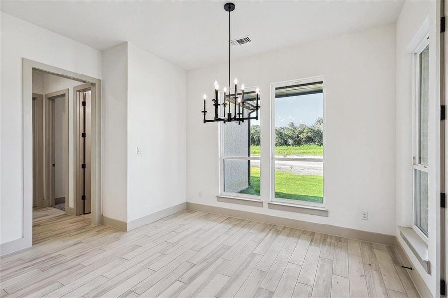 Unfurnished dining area featuring a healthy amount of sunlight, a notable chandelier, and light wood-type flooring