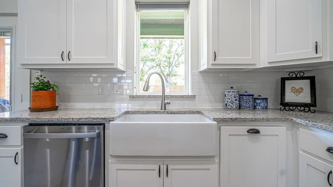 Kitchen with white cabinetry, light stone counters, backsplash, stainless steel dishwasher, and sink