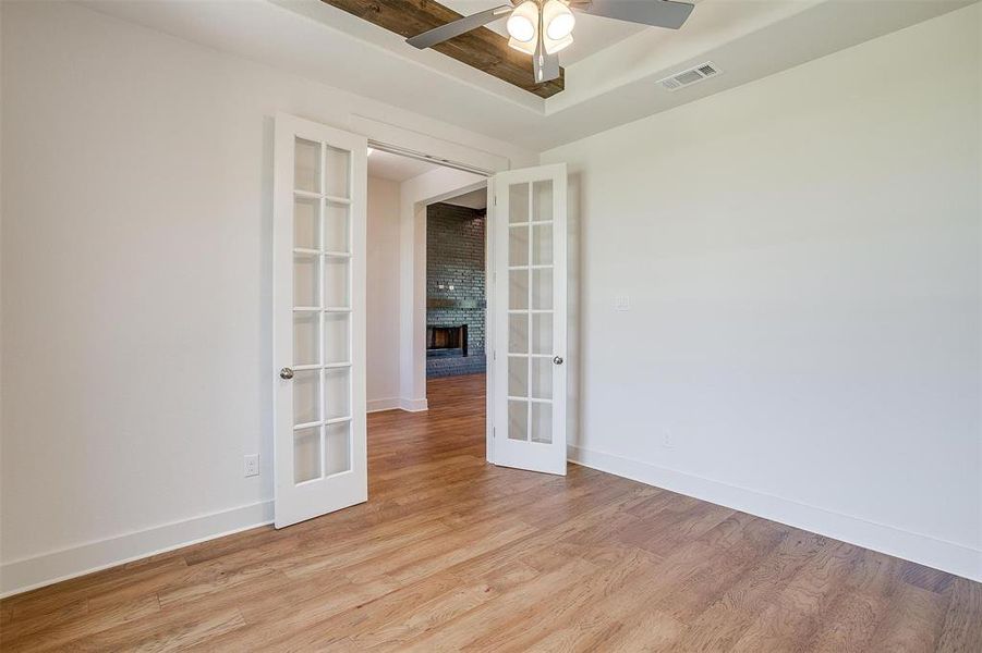 Spare room with ceiling fan, french doors, a fireplace, brick wall, and hardwood / wood-style flooring