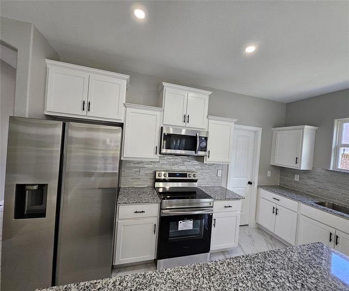 Kitchen featuring stone counters, stainless steel appliances, decorative backsplash, and white cabinetry