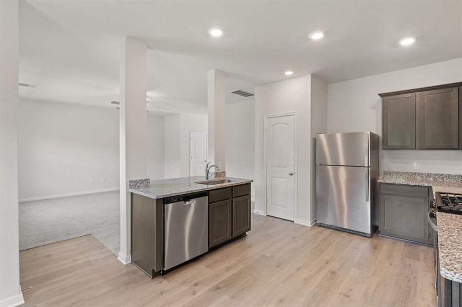 Kitchen with dark brown cabinetry, light wood-type flooring, sink, stainless steel appliances, and light stone countertops