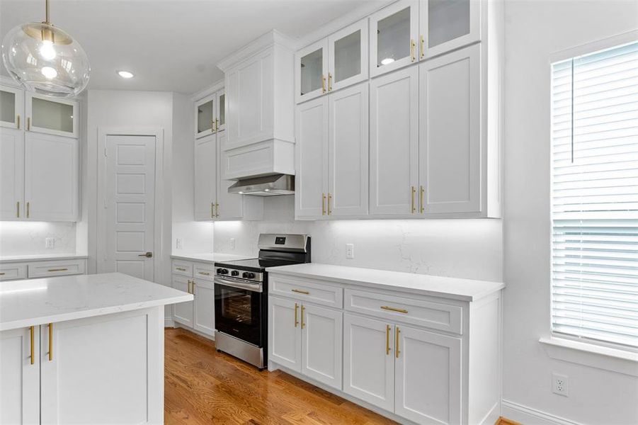 Kitchen featuring light stone counters, stainless steel stove, pendant lighting, light hardwood / wood-style floors, and white cabinets