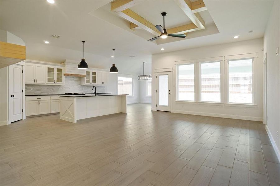 Unfurnished living room with ceiling fan, sink, light wood-type flooring, and a tray ceiling