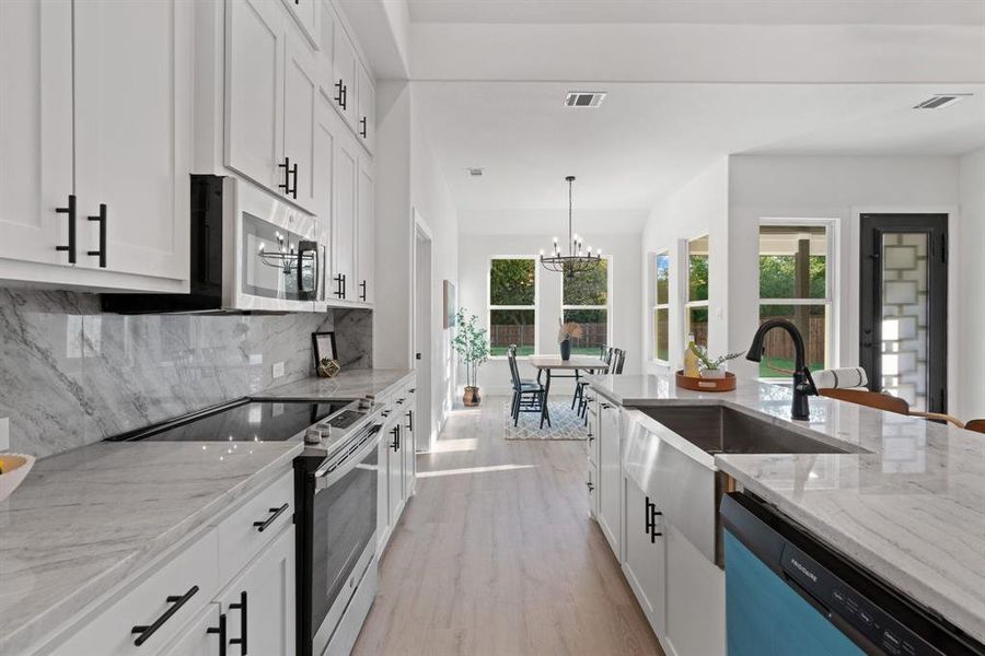 Kitchen featuring white cabinets, appliances with stainless steel finishes, a notable chandelier, light stone countertops, and light hardwood / wood-style floors