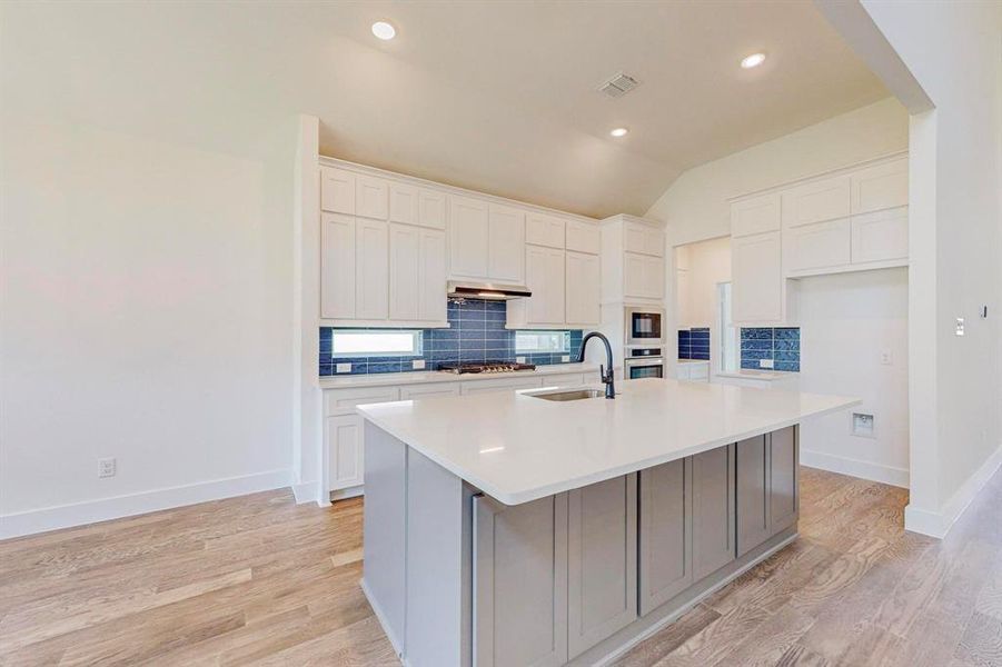 Kitchen featuring white cabinetry, light hardwood / wood-style flooring, stainless steel appliances, and a center island with sink