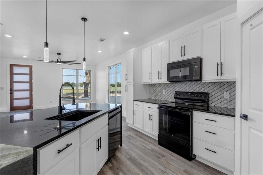 Kitchen with light hardwood / wood-style floors, decorative light fixtures, sink, black appliances, and white cabinetry