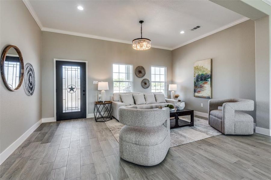 Living room with crown molding, a chandelier, and light hardwood / wood-style flooring