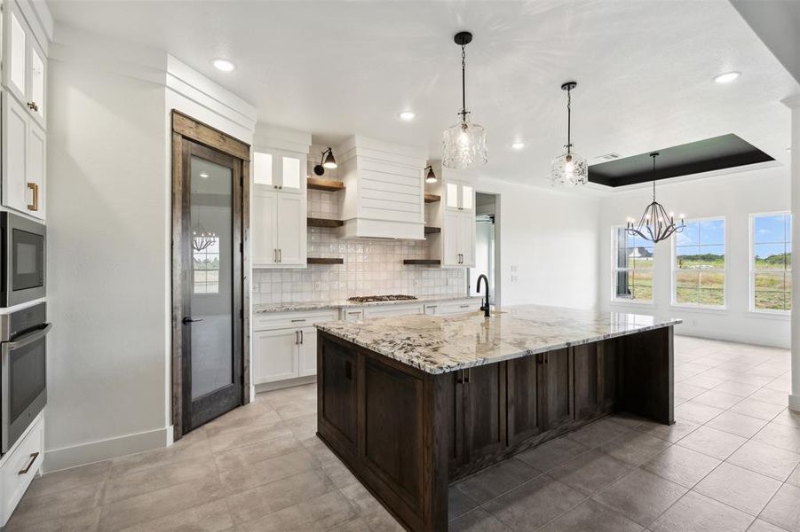 Kitchen with appliances with stainless steel finishes, white cabinets, backsplash, an island with sink, and light tile patterned flooring