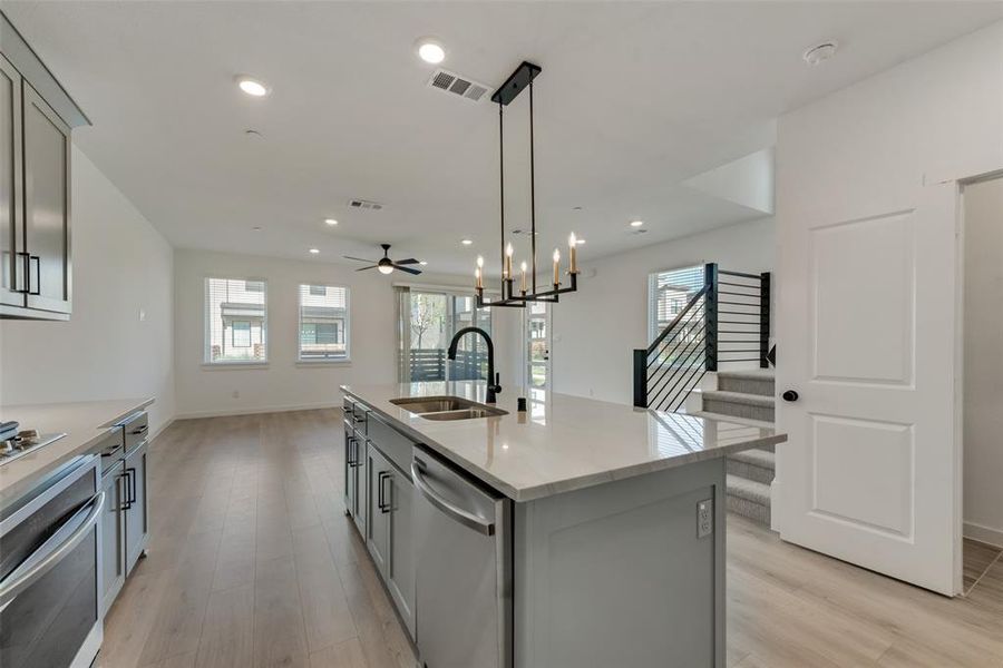 Kitchen featuring stainless steel appliances, sink, a kitchen island with sink, light wood-type flooring, and ceiling fan with notable chandelier