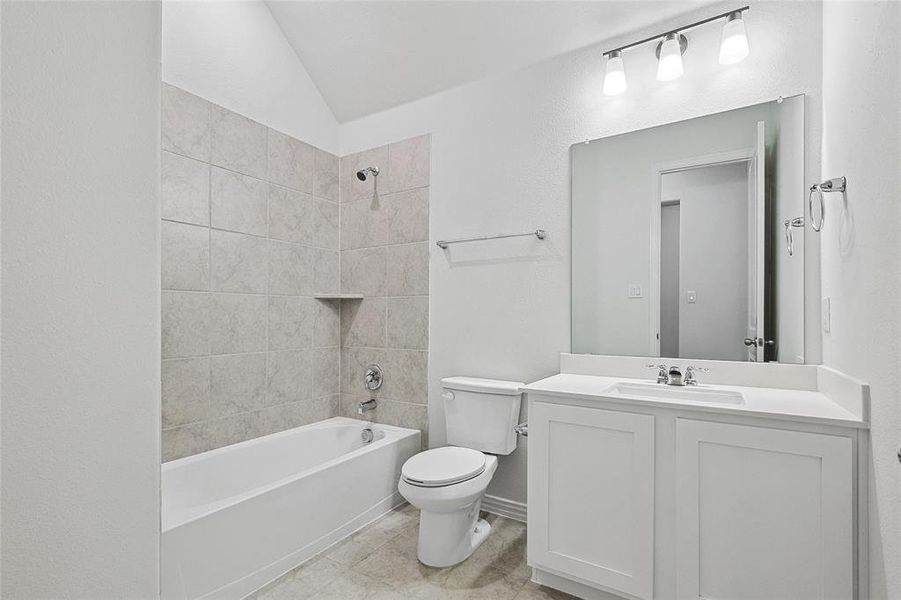 Full bathroom with vanity, tile patterned floors, tiled shower / bath, toilet, and lofted ceiling