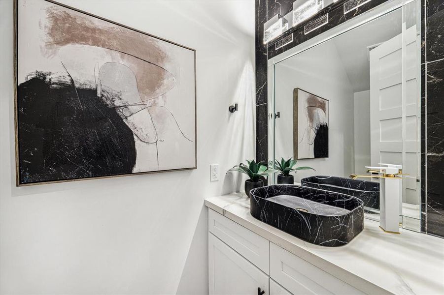 This stylish powder bathroom, conveniently located near the mudroom, laundry room, and garage entryway, features a black marble surround and a modern bowl sink.