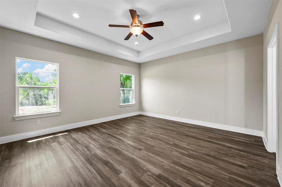 Unfurnished room with dark hardwood / wood-style flooring, ceiling fan, and a raised ceiling