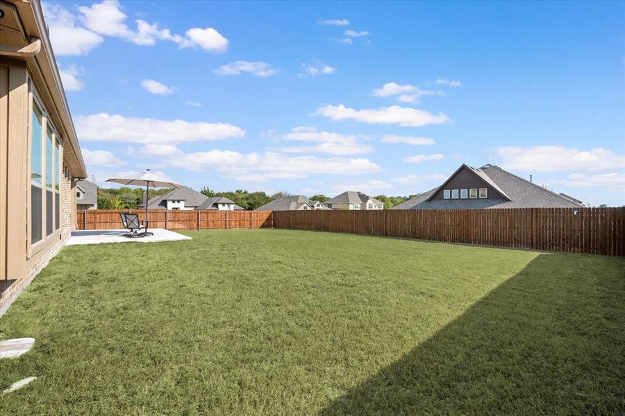 View of the large backyard. Stained 6 foot fencing has steel posts. Patio is partially covered.