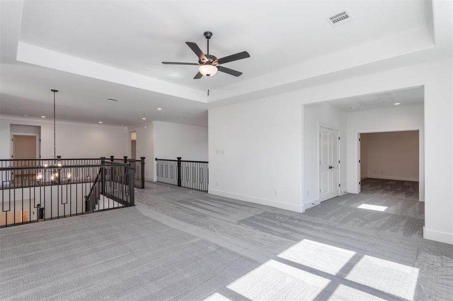 Carpeted empty room featuring a tray ceiling and ceiling fan with notable chandelier