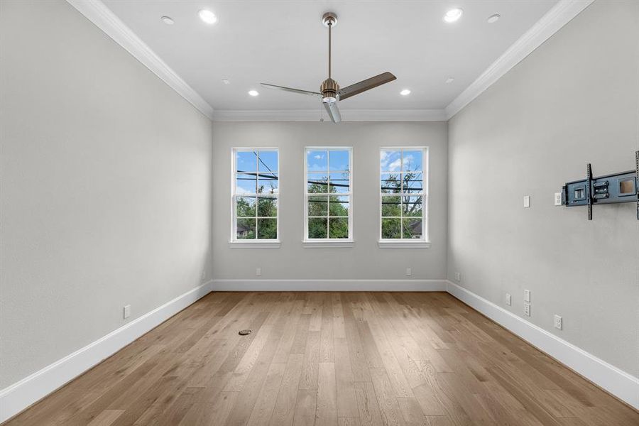 The family room offers high ceilings complimented by crown molding, recessed lighting and a modern ceiling fan, creating a bright and airy atmosphere. The neutral paint palette complements the stunning wood floors, while large windows invite an abundance of natural light to flood the space throughout the day.