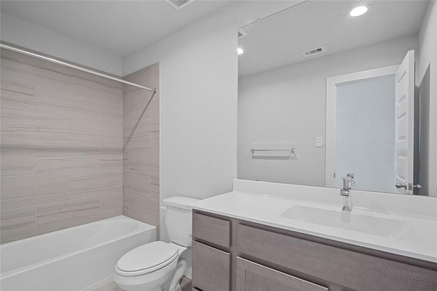 Secondary bath features tile flooring, bath/shower combo with tile surround, stained wood cabinets, beautiful light countertops, mirror, sleek fixtures and modern finishes.