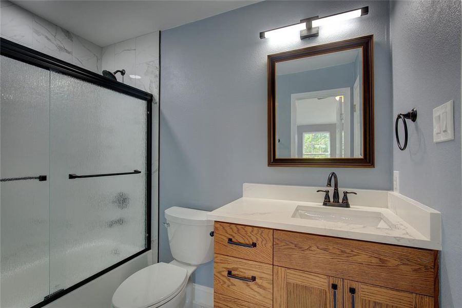 Upstairs bathroom with vanity, bath / shower combo with glass door, and toilet is accessible from bedroom 2 and the hallway