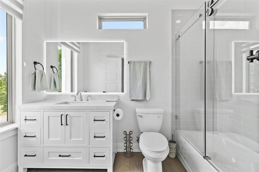 Full bathroom featuring shower / bath combination with glass door, a healthy amount of sunlight, vanity, and toilet