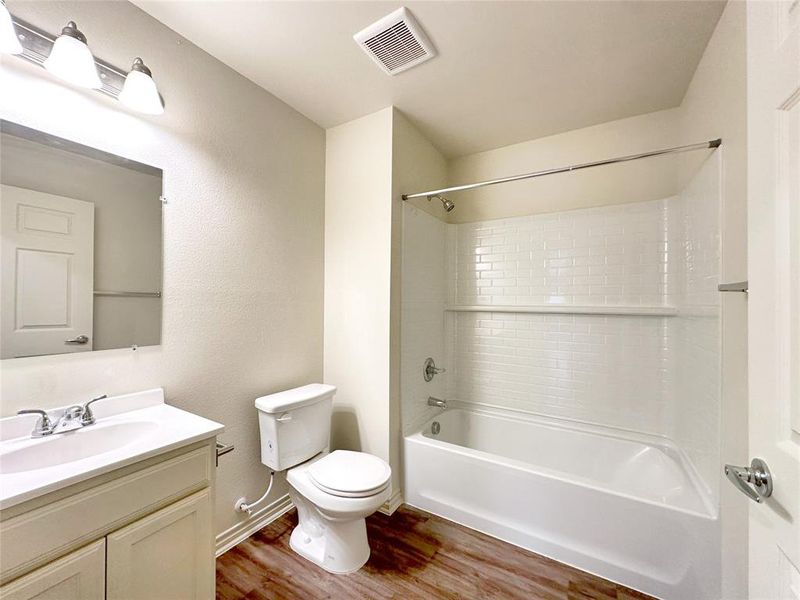 Full bathroom with wood-type flooring, tiled shower / bath, vanity, and toilet