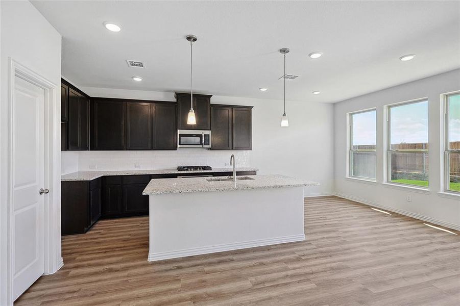 Kitchen featuring decorative light fixtures, tasteful backsplash, an island with sink, sink, and light hardwood / wood-style floors