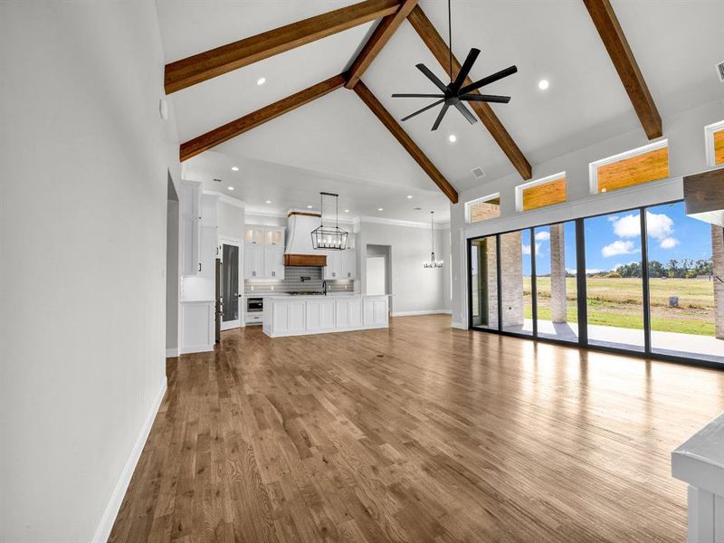 Unfurnished living room featuring beam ceiling, sink, light wood-type flooring, high vaulted ceiling, and ceiling fan with notable chandelier