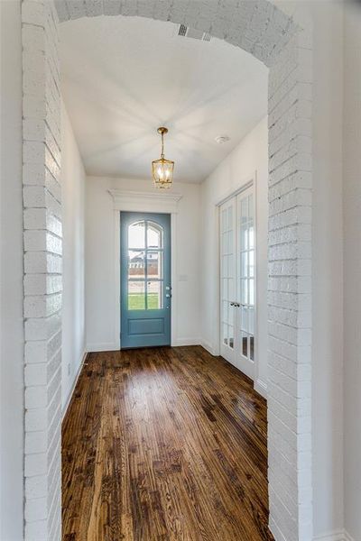 Foyer with brick wall, french doors, hardwood / wood-style floors, and an inviting chandelier