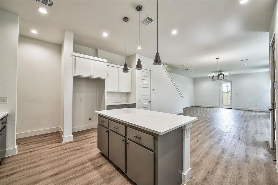 Kitchen with a notable chandelier, light hardwood / wood-style floors, hanging light fixtures, a center island, and white cabinets