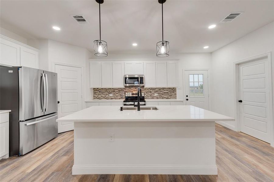 Kitchen featuring appliances with stainless steel finishes, light hardwood / wood-style flooring, a kitchen island with sink, and sink