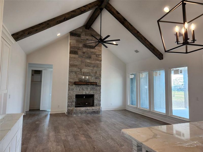 Unfurnished living room with a stone fireplace, high vaulted ceiling, an inviting chandelier, beamed ceiling, and wood-type flooring