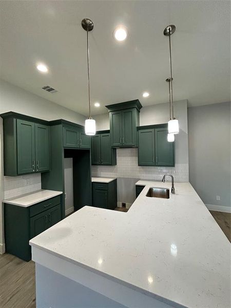 Kitchen featuring kitchen peninsula, decorative light fixtures, sink, and dark wood-type flooring