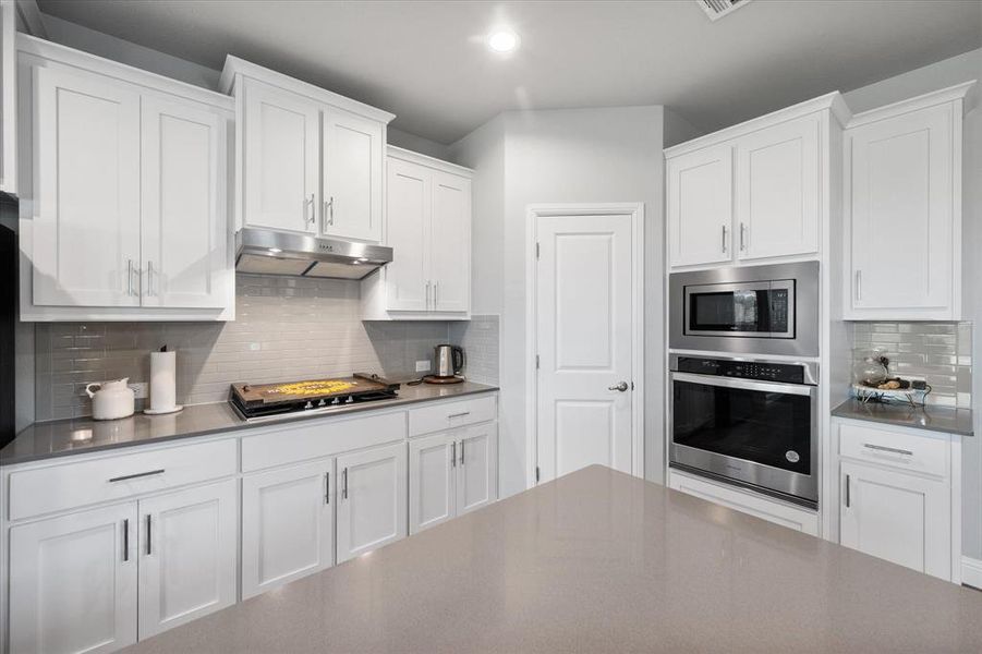 Kitchen featuring decorative backsplash, stainless steel appliances, and white cabinetry