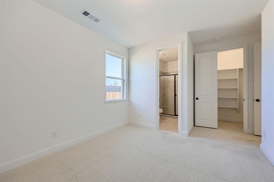 Unfurnished bedroom featuring a spacious closet, light carpet, ensuite bathroom, and a closet