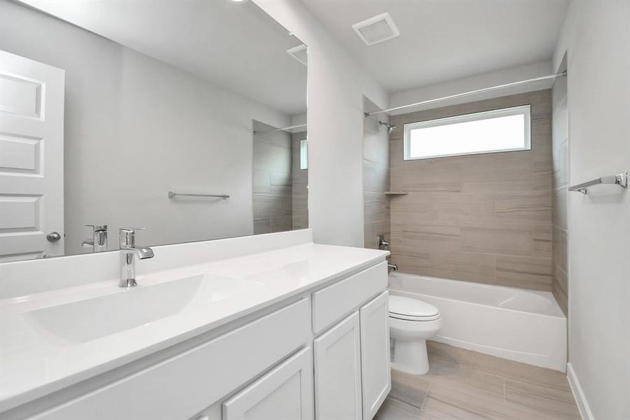 Secondary bath  showcases stylish tile flooring, a bath/shower combo with an elegant tile surround, and light-stained wood cabinets.