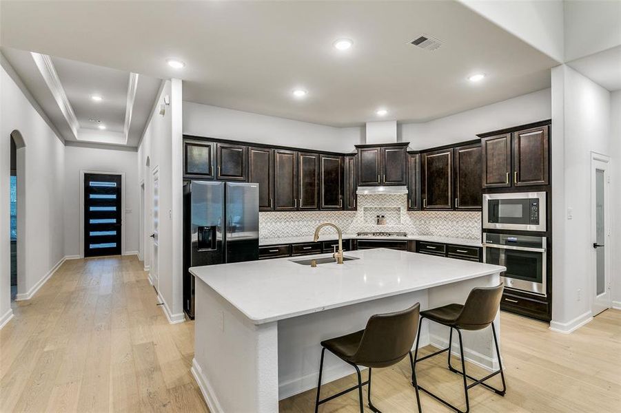 Kitchen with sink, light hardwood / wood-style floors, stainless steel appliances, a breakfast bar area, and a center island with sink